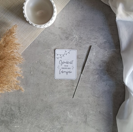 DIY-Geburtstagskarte mit Wunderkerze und der Aufschrift „Glückslicht für ein strahlendes neues Lebensjahr“, dekoriert mit Kerze, Pampasgras und Leinenstoff auf hellem Untergrund.