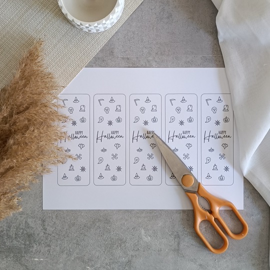 DIY-Halloweenkarte mit aufgeklebten Wunderkerzen auf grauem Untergrund, umgeben von herbstlicher Deko und Bastelutensilien