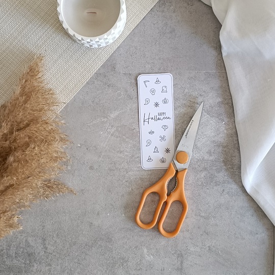 DIY-Halloweenkarte mit aufgeklebten Wunderkerzen auf grauem Untergrund, umgeben von herbstlicher Deko und Bastelutensilien