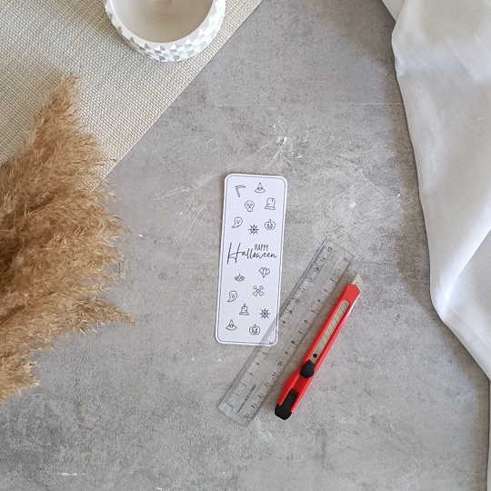 DIY-Halloweenkarte mit aufgeklebten Wunderkerzen auf grauem Untergrund, umgeben von herbstlicher Deko und Bastelutensilien