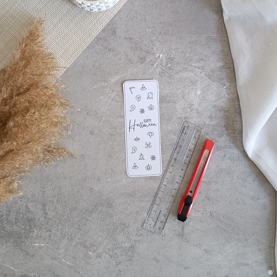 DIY-Halloweenkarte mit aufgeklebten Wunderkerzen auf grauem Untergrund, umgeben von herbstlicher Deko und Bastelutensilien