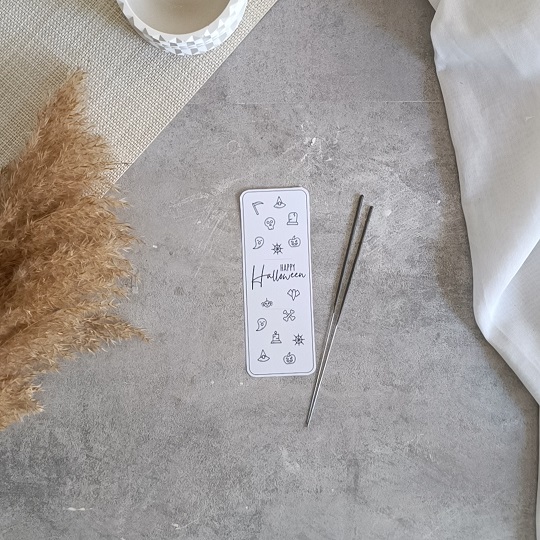DIY-Halloweenkarte mit aufgeklebten Wunderkerzen auf grauem Untergrund, umgeben von herbstlicher Deko und Bastelutensilien
