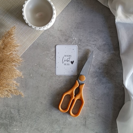 Minimalistische DIY-Neujahrskarte mit Wunderkerze und dem Text „Ein kleines Licht für 2024“, dekoriert mit Kerze, Trockenblumen und Stoff auf hellgrauem Untergrund.