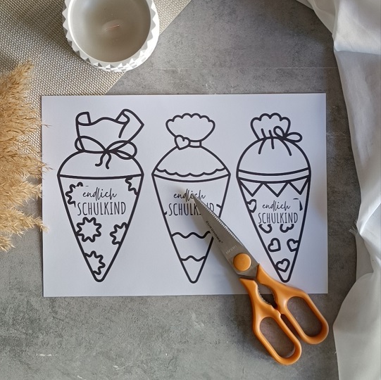 DIY-Karte in Schultütenform mit rotem Bleistift und dem Schriftzug „Endlich Schulkind“, dekoriert mit Kerze, Pampasgras und Stoff auf grauem Untergrund.