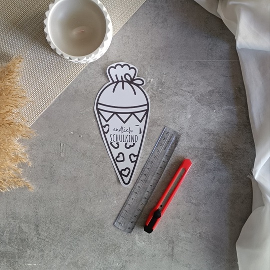 DIY-Schultüten-Karte in Schultütenform mit rotem Bleistift und dem Schriftzug „Endlich Schulkind“, dekoriert mit Kerze, Pampasgras und Stoff auf grauem Untergrund.