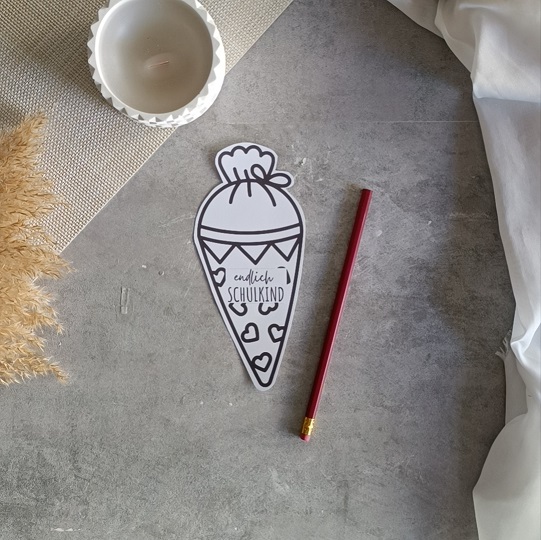 DIY-Schultüten-Karte in Schultütenform mit rotem Bleistift und dem Schriftzug „Endlich Schulkind“, dekoriert mit Kerze, Pampasgras und Stoff auf grauem Untergrund.