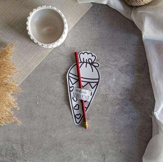 DIY-Schultüten-Karte in Schultütenform mit rotem Bleistift und dem Schriftzug „Endlich Schulkind“, dekoriert mit Kerze, Pampasgras und Stoff auf grauem Untergrund.