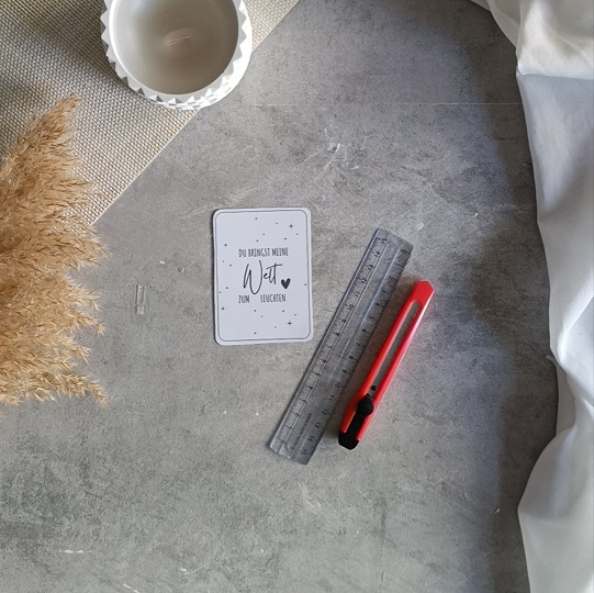 DIY-Karte mit Wunderkerze und der Aufschrift „Du bringst meine Welt zum Leuchten“, liebevoll dekoriert mit Kerze, Pampasgras und hellem Stoff auf Betonoptik-Hintergrund.
