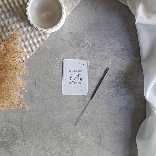 DIY-Karte mit Wunderkerze und der Aufschrift „Du bringst meine Welt zum Leuchten“, liebevoll dekoriert mit Kerze, Pampasgras und hellem Stoff auf Betonoptik-Hintergrund.